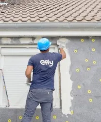 Artisan de dos avec t shirt effy portant un casque bleu et realisant l isolation des murs par l exterieur